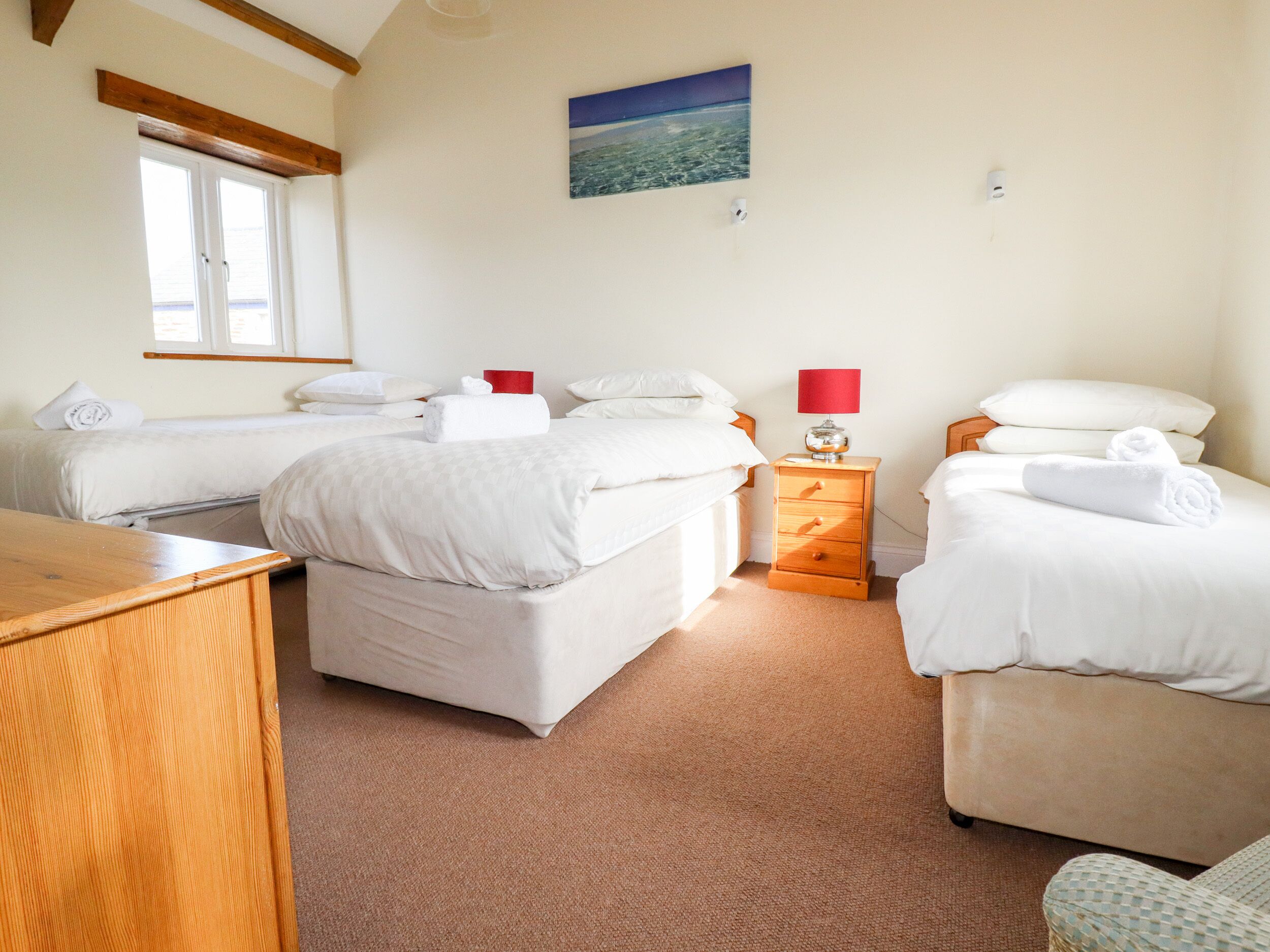 A hotel room with two beds, a wooden desk, a nightstand with a lamp, and a painting on the wall.