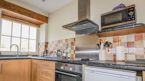 Eine moderne Küche mit Holzschränken, einem Geschirrspüler von Bosch, einem Backofen von Bosch, einer Mikrowelle und einer Edelstahl-Dunstabzugshaube.