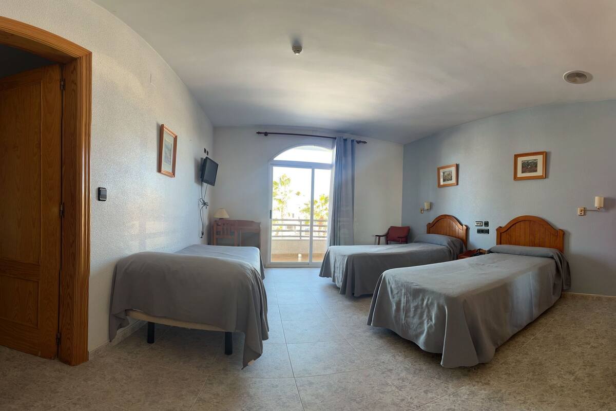 Habitación de hotel con dos camas, una puerta de madera, un balcón con vistas y un ventilador de techo.