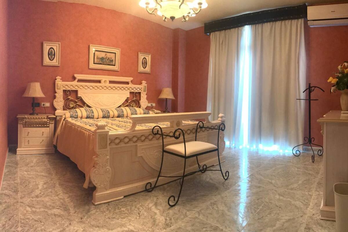 Un dormitorio con una cama grande, dos mesitas de noche, un aparador, una silla y un espejo.