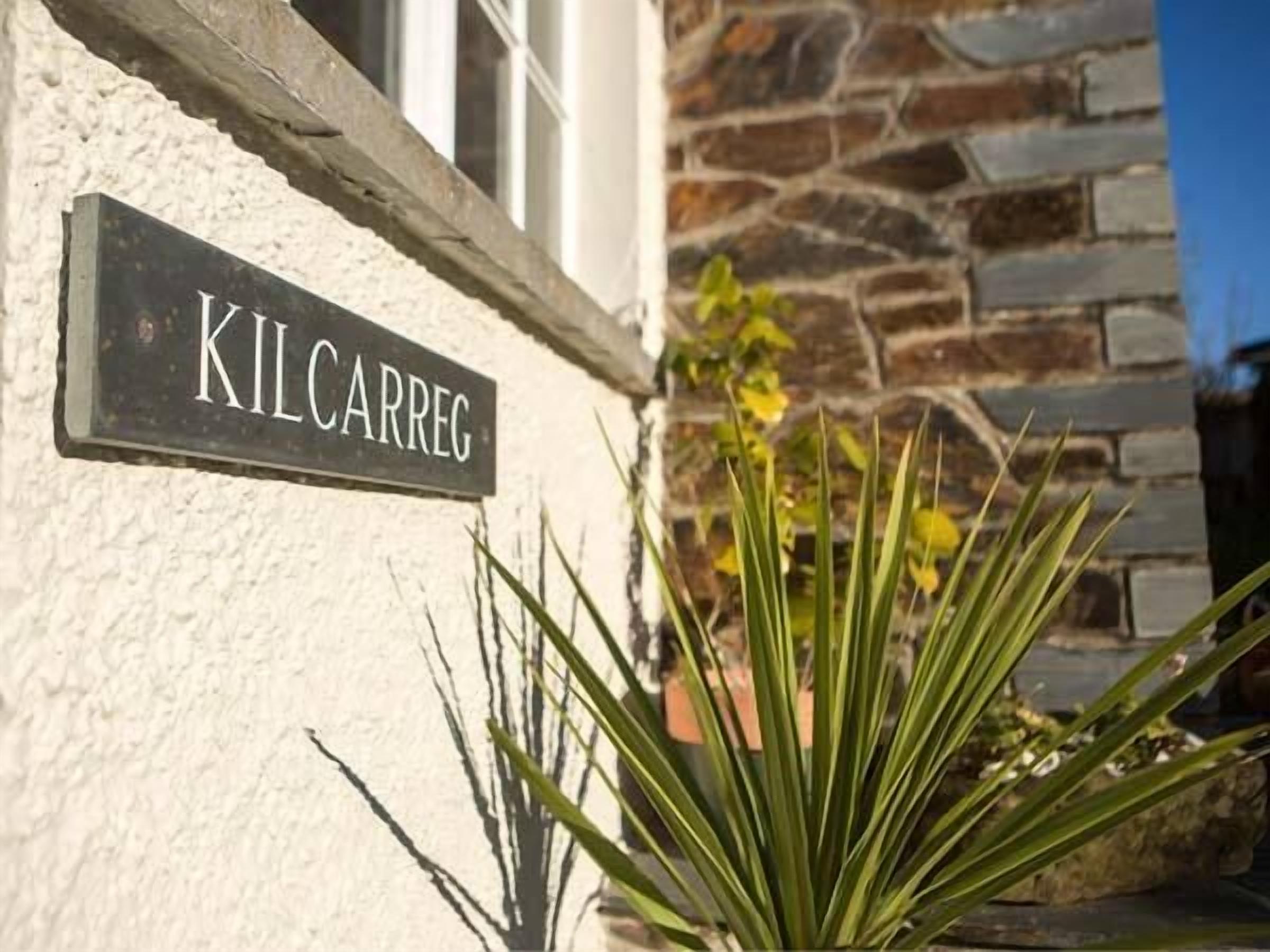 Una señal de calle que dice "KILCARREG" montada en un edificio de fachada de piedra y una planta al frente.