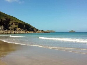 Une plage avec une eau d’un bleu limpide, un rivage sablonneux et des falaises rocheuses.