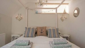 Ein Schlafzimmer mit einem Bett, zwei Nachttischen, einer Chandelüster, einem Fenster mit Jalousien und einem an der Wand befestigten Spiegel.