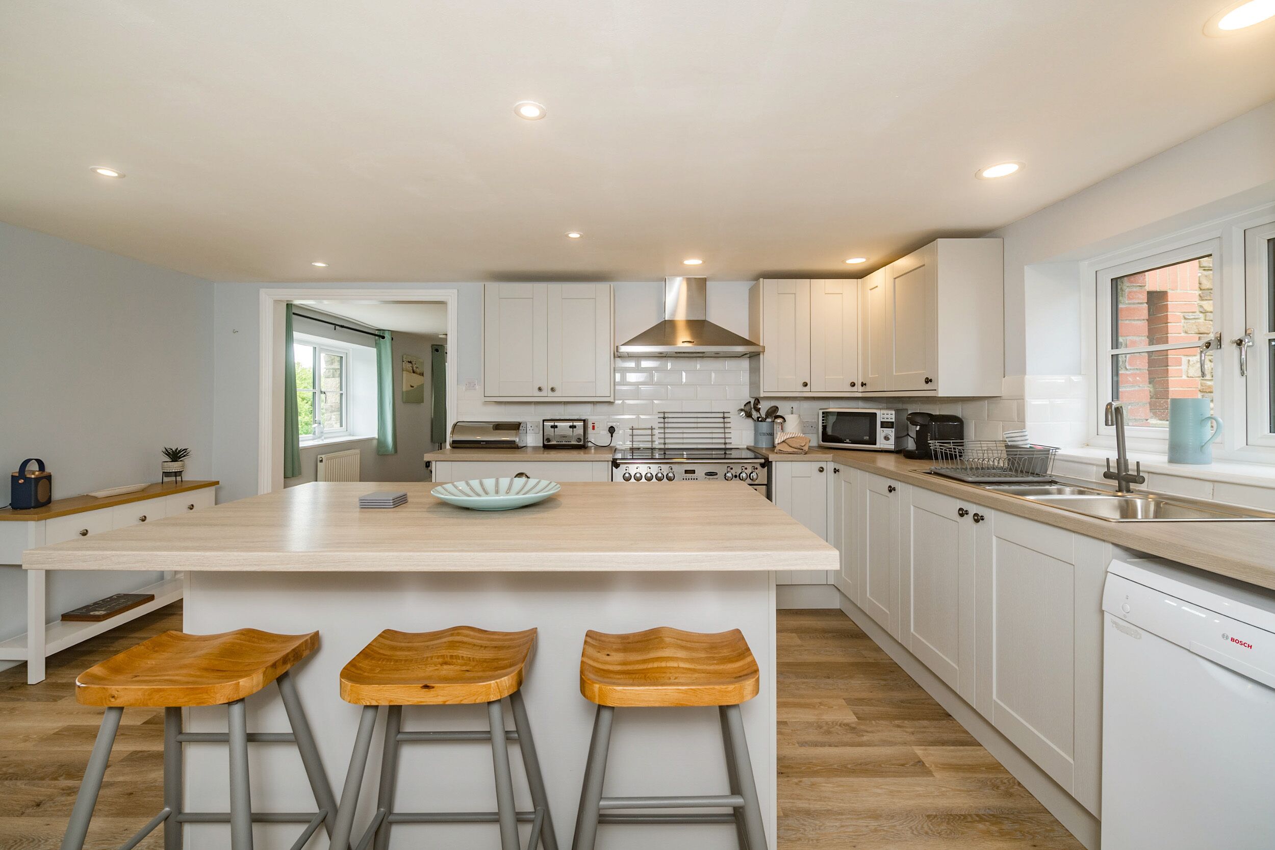 A modern kitchen with a large island, white cabinetry, and a Bosch dishwasher.