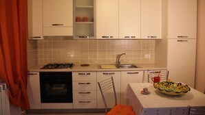 Una cocina funcional con armarios blancos, estufa a gas, lavavajillas y pileta.