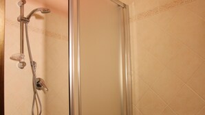 Un baño con ducha de mampara de vidrio, lavabo sobre pedestal y paredes con azulejos.