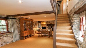 A spacious living area with a stone fireplace, a wooden cabinet, and a staircase leading to an upper level. - Barn Cottage (Hayle)