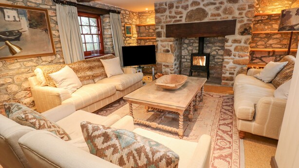 A cozy living room with stone walls, a fireplace, and comfortable seating. - Barn Cottage (Hayle)