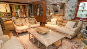 A cozy living room with a stone wall, a fireplace, and a dining area in the background. - Barn Cottage (Hayle)