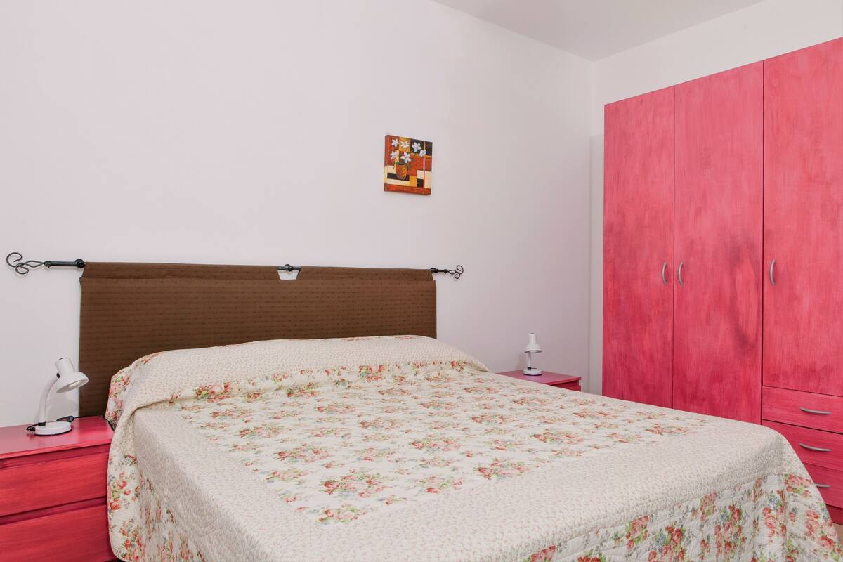 Un dormitorio con una cama, un armario rojo, una mesita de noche y una lámpara de pared.