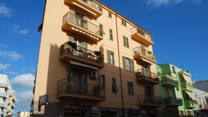 A multi-story building with balconies, storefronts, and parked cars.