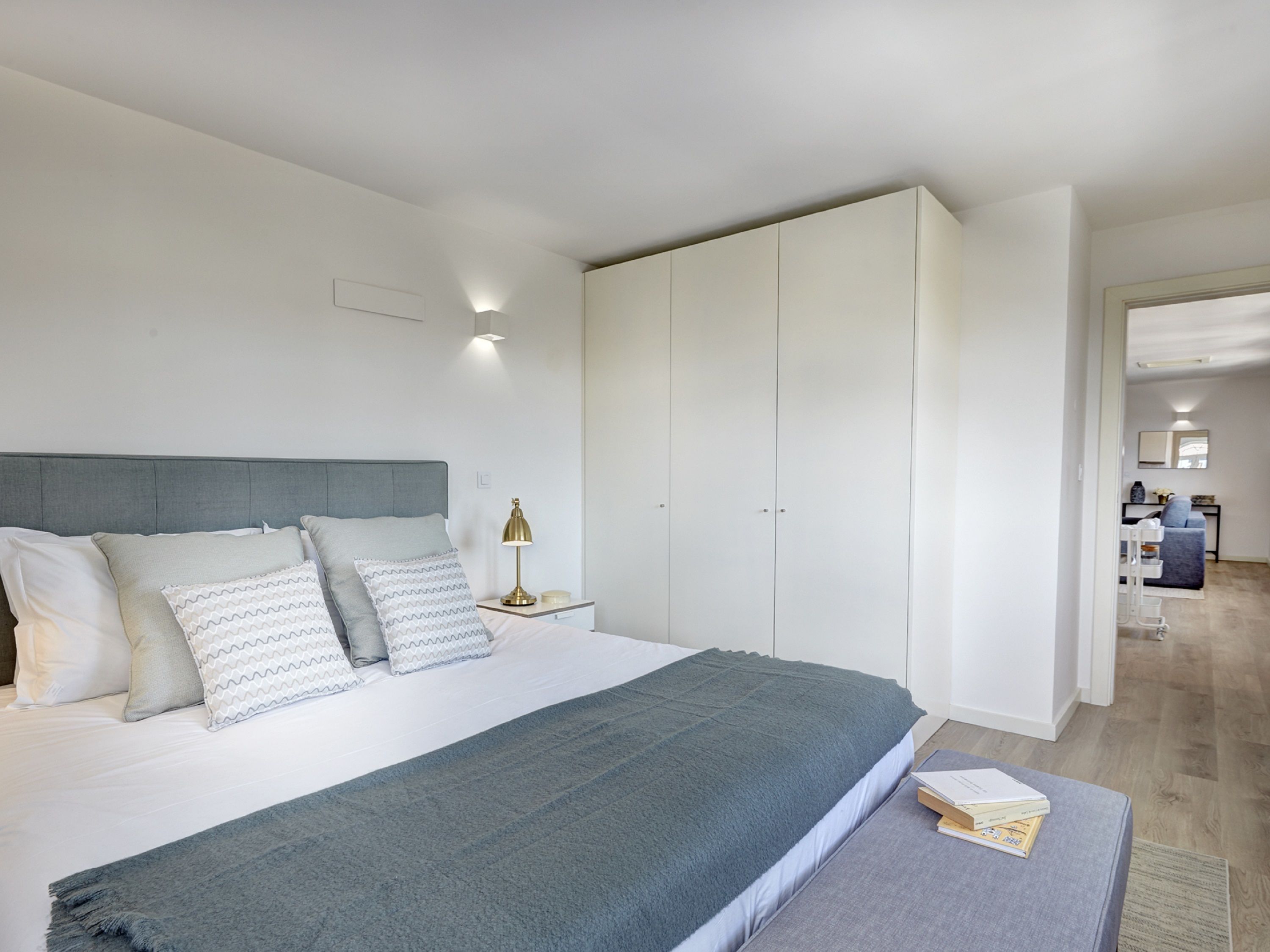 A modern bedroom with a bed, bedside tables, a wardrobe, and a view into the living area.