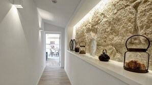 A hallway with a stone wall, a shelf with decorative items, and a view into a dining area.