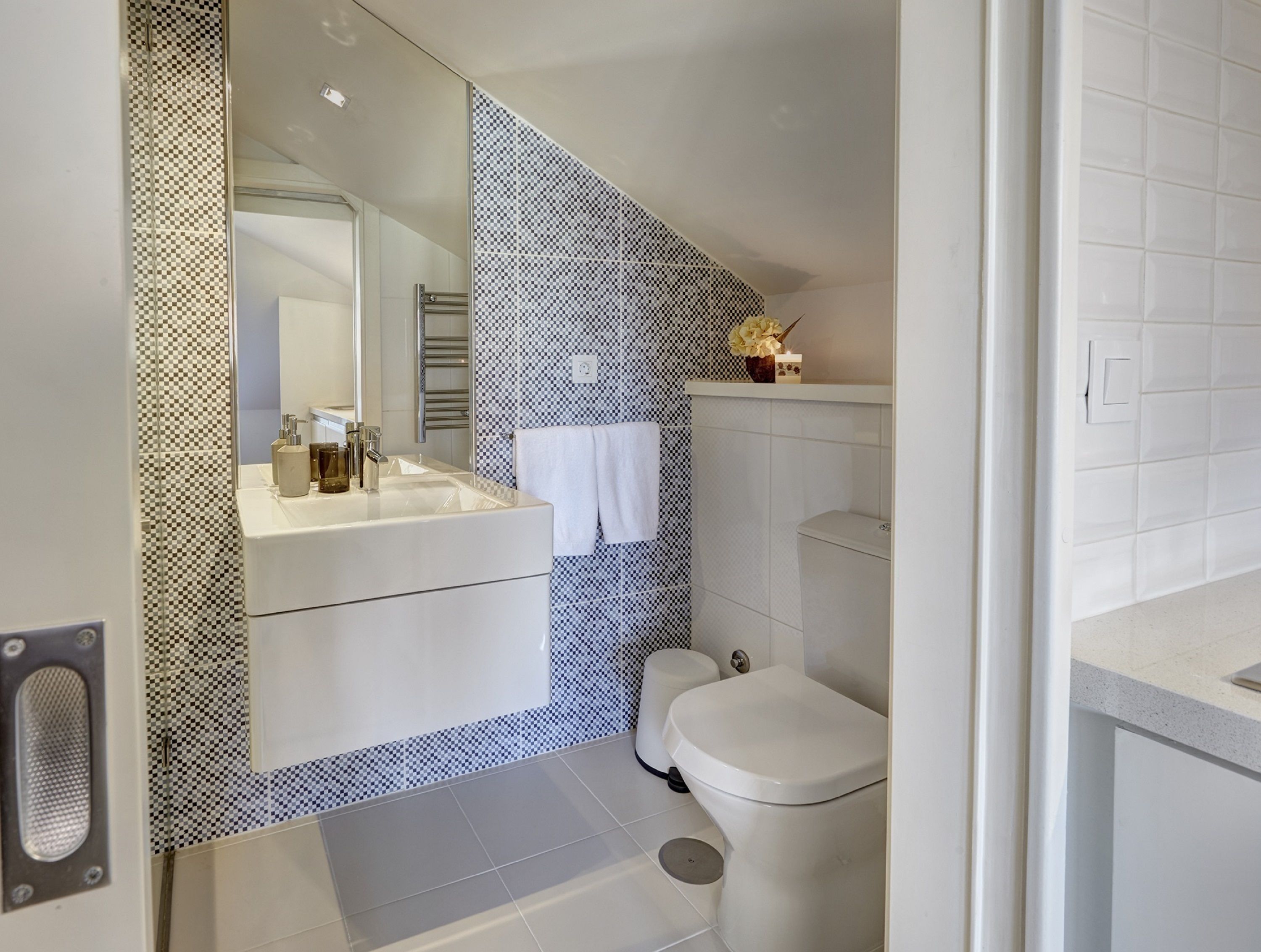 A modern bathroom with a checkered tile backsplash, a white sink, a mirror, and a toilet.