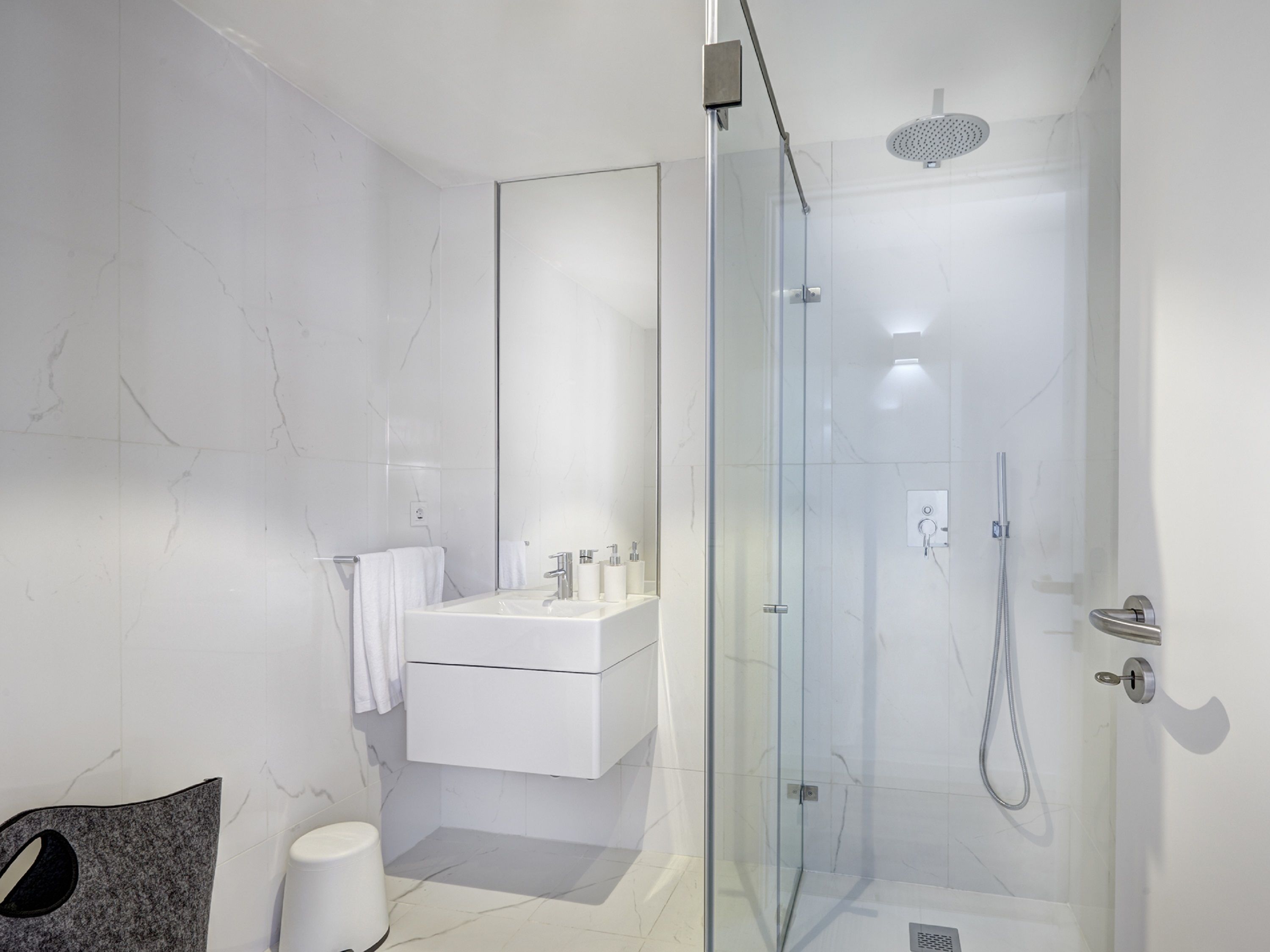 A modern bathroom with a glass-enclosed shower, a white vanity with a mirror, and a towel rack.