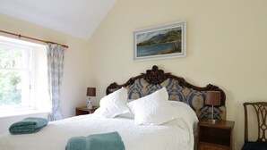 A neatly made bed with white and teal towels, a wooden headboard, a nightstand with a lamp, and a framed painting on the wall. - Bannatyne Lodge (Blairgowrie)