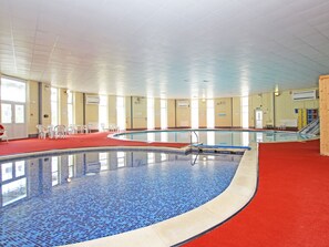 An indoor swimming pool with clear blue tiles, surrounded by white chairs and a red carpeted area. - Dartmoor Valley Lodge 10 (Gunnislake)