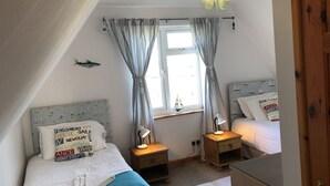 Ein Schlafzimmer mit zwei Betten, einem Fenster mit Vorhängen, einer Nachttischlampe und einem kleinen Tisch.