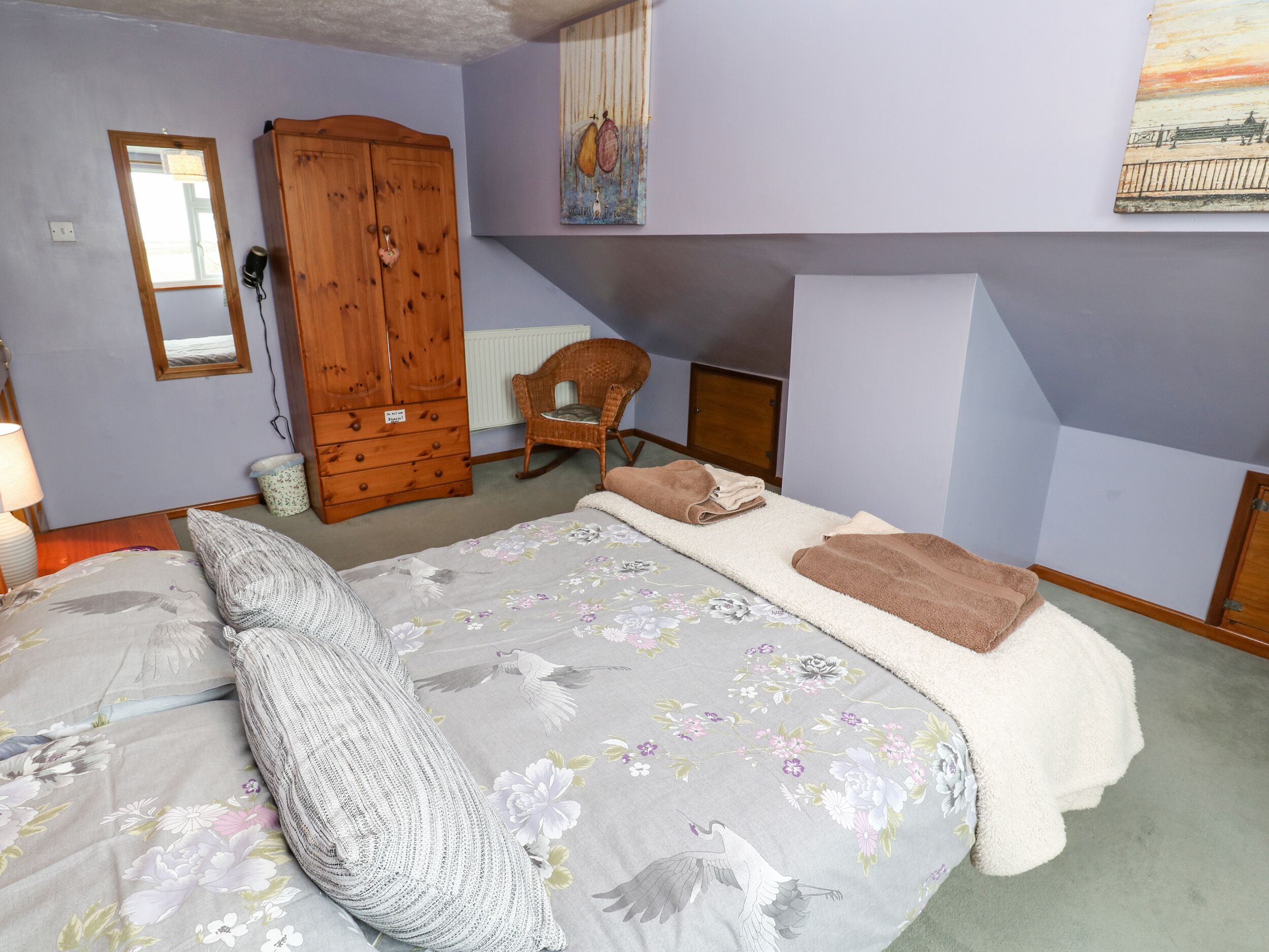 Une chambre à coucher avec un lit, une armoire en bois, une chaise et un tableau accroché au mur.