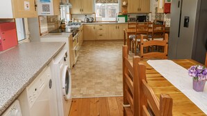 Una cucina con mobili in legno, una lavatrice, un tavolo da pranzo con sedie e un frigorifero.