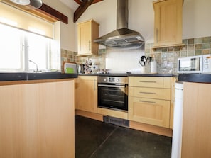 A compact kitchen with wooden cabinets, a stainless steel range hood, a built-in oven, and a microwave. - Wheal Kitty (Newquay)