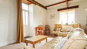 En hyggelig stue med en beige sofa, træstole, et lille bord og et vindue med gardiner.