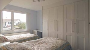 Un dormitorio con dos camas, una ventana, un armario y un ventilador de techo.