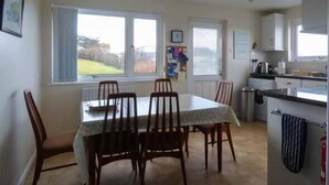 Un comedor con una mesa y sillas, una ventana con persianas, un radiador y una zona de cocina con armarios y un hervidor.