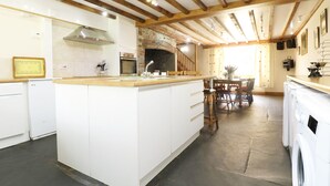 A modern kitchen with a central island, wooden beams, and a stone fireplace. - Eastcott Farmhouse (Holsworthy)
