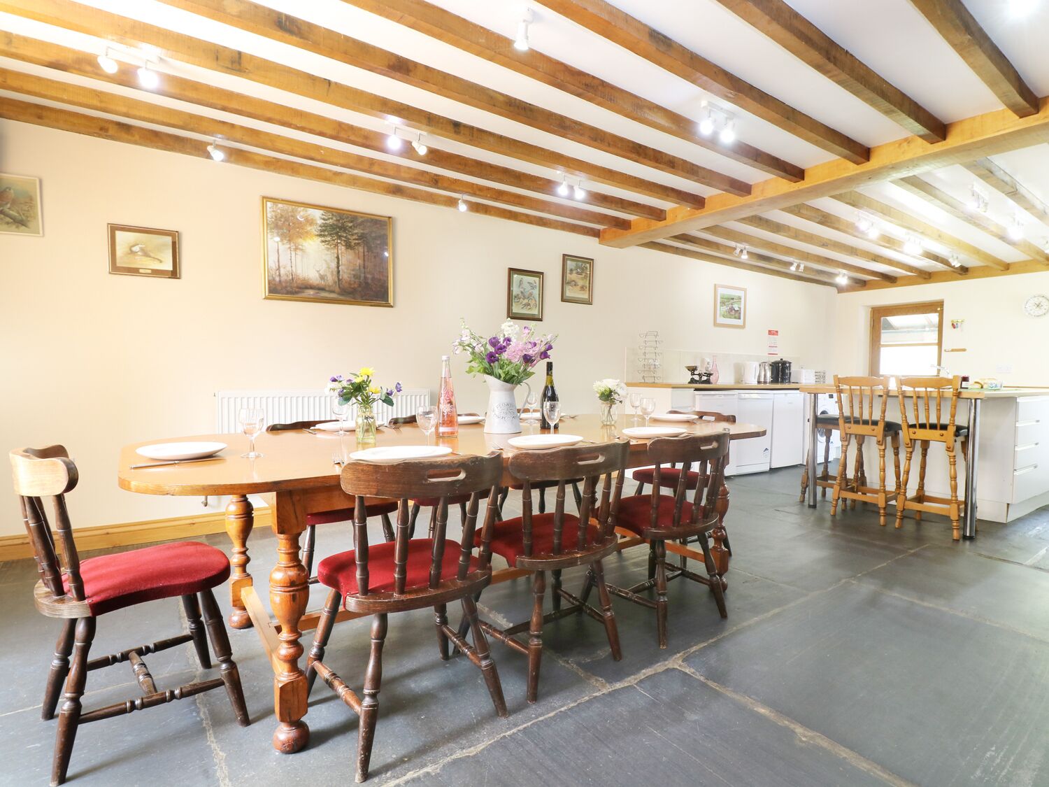 Un comedor con una mesa y sillas de madera, una cocina al fondo y obras de arte en las paredes.