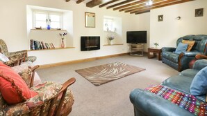A living room with exposed wooden beams, a flat-screen TV, a sofa, a chair, and a rug. - Eastcott Farmhouse (Holsworthy)