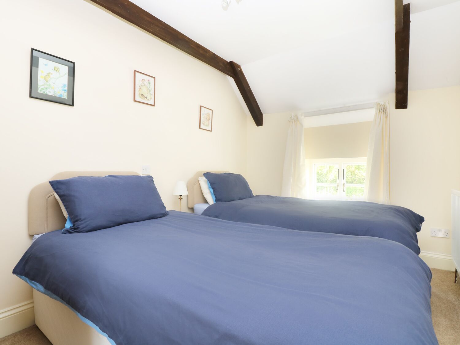 Una habitación con dos camas, una ventana con cortinas y un techo con vigas a la vista.