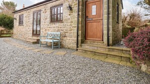 A stone cottage with a wooden door and windows, a bench outside, and a gravel driveway. - Brocks Barn (Bodmin)