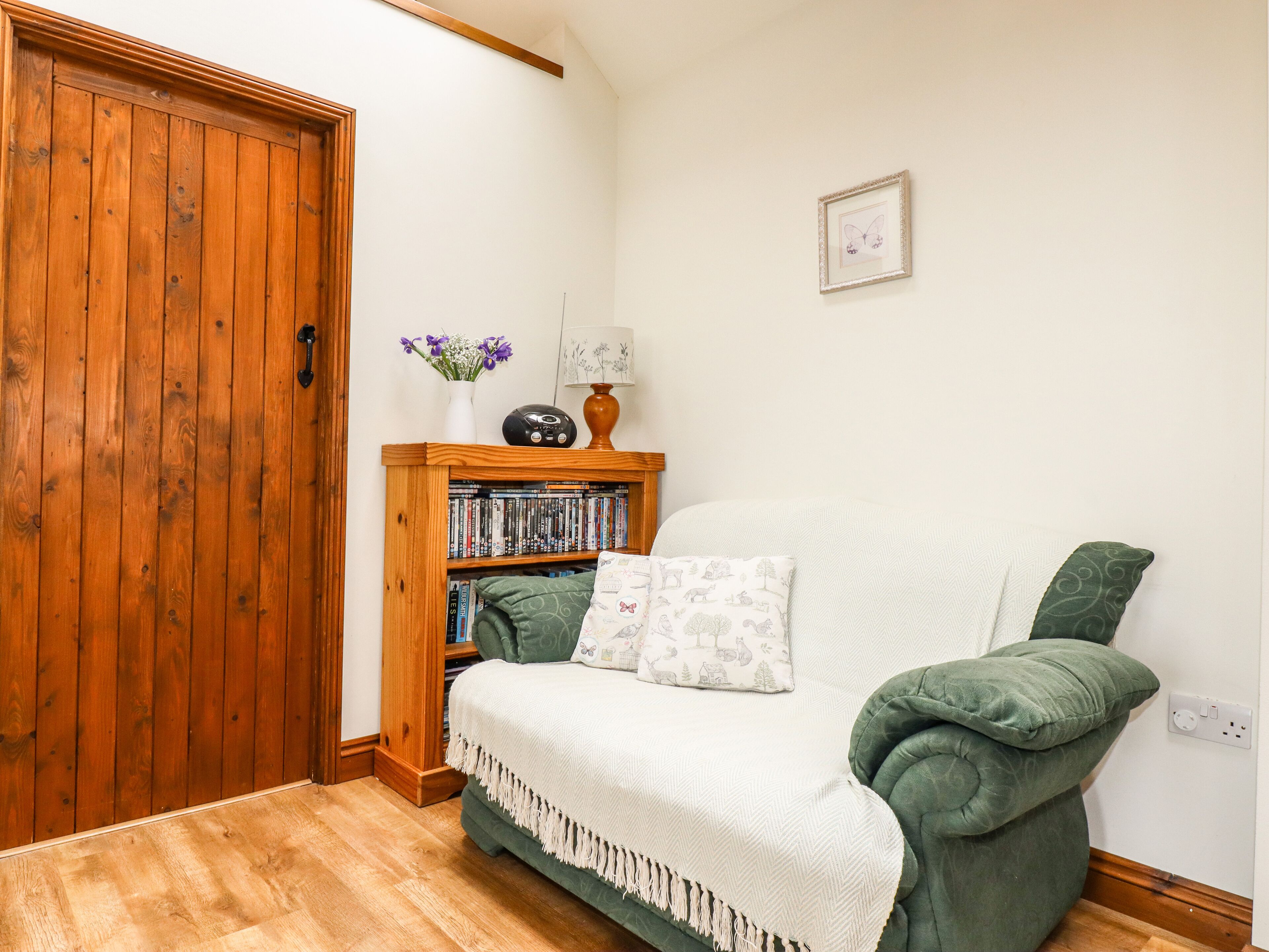 A cozy room with a wooden door, a bookshelf, a green sofa, and a framed picture on the wall.