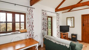 A cozy room with a wooden dining table, a green sofa, a television, and a fireplace. - Brocks Barn (Bodmin)