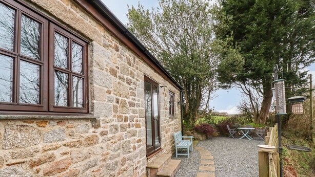 A stone building with a gravel patio, a wooden bench, and a bird feeder. - Brocks Barn (Bodmin)