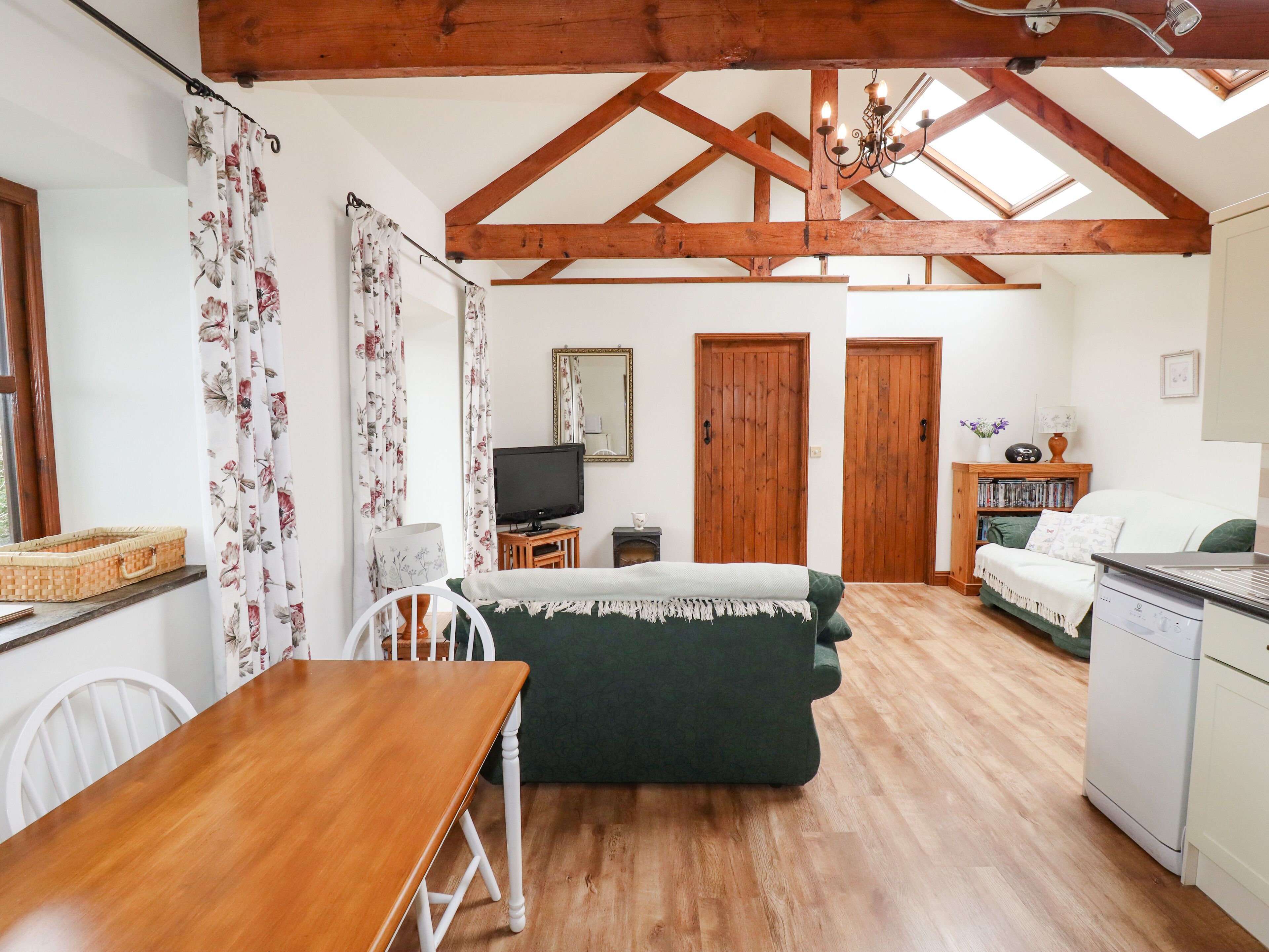 A cozy room with a wooden ceiling, a dining table with chairs, a green sofa, a television on a wooden stand, and a bookshelf.