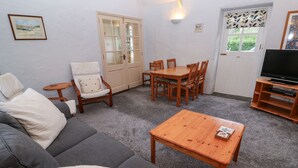 A living room with a sofa, a wooden coffee table, a dining table with chairs, a TV stand, and a door with a window.