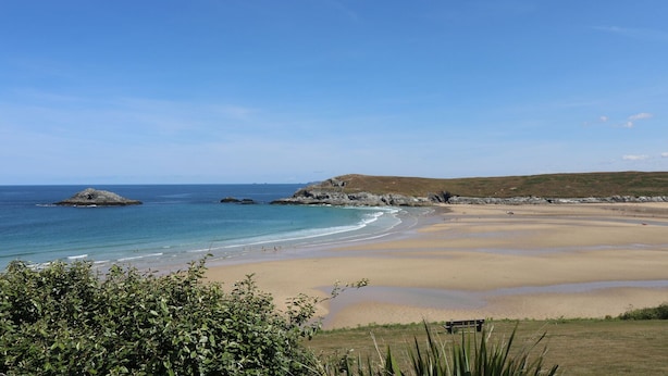 A coastal landscape with a sandy beach, rocky outcrops, and a clear blue sky.