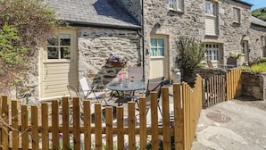 A stone house with a wooden fence, a patio with outdoor furniture, and a small garden area.