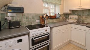 A kitchen with a washing machine, two ovens, a toaster, and a sink.
