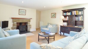 A living room with a fireplace, a television, a sofa, a coffee table, and a bookshelf. - Farm Cottage (Hayle)