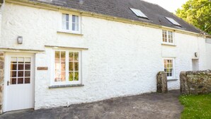A white building with a stone wall, a door, and two windows. - Farm Cottage (Hayle)