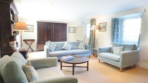 A living room with a sofa, armchairs, a coffee table, and a bookshelf. - Farm Cottage (Hayle)
