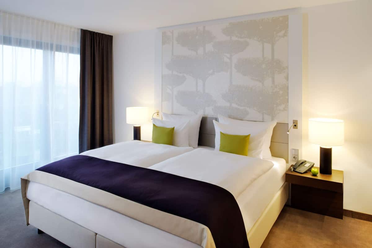 A hotel room with a large bed, two bedside tables with lamps, a telephone, and a fruit on one table.