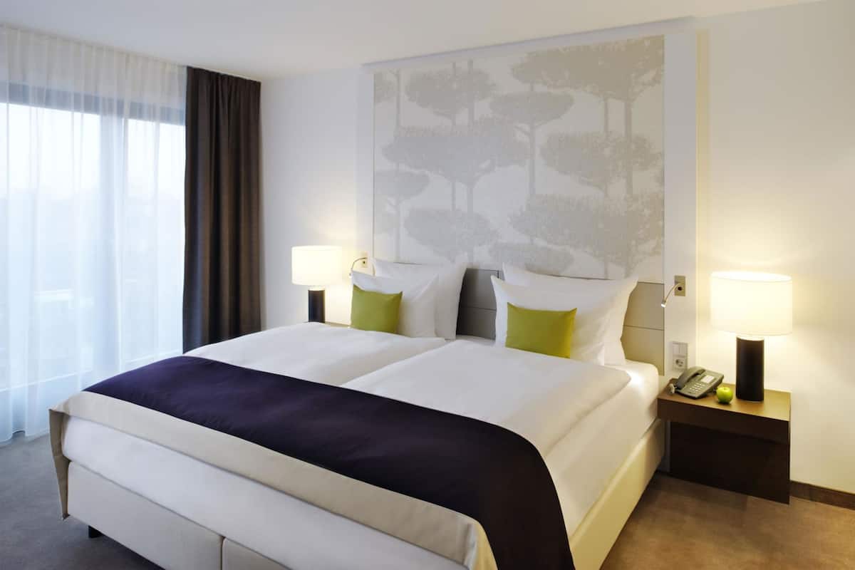 A hotel room with a large bed, two bedside tables, a telephone, and a lamp on one table.