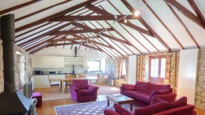 A cozy living area with a fireplace, red sofas, and a kitchen in the background. - The Granary (Hayle)