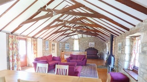 A rustic interior with a wooden dining table, purple sofas, and a stone fireplace. - The Granary (Hayle)