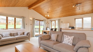 A cozy living room with a wooden ceiling, a sofa set, a wooden coffee table, and a view of the outdoors through large windows. - High Tide (Wadebridge)