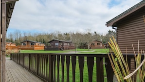 A wooden deck with a view of several cabins and a grassy area. - High Tide (Wadebridge)